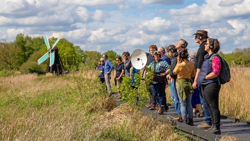 A group of visitors stood in a line listening with a microphone